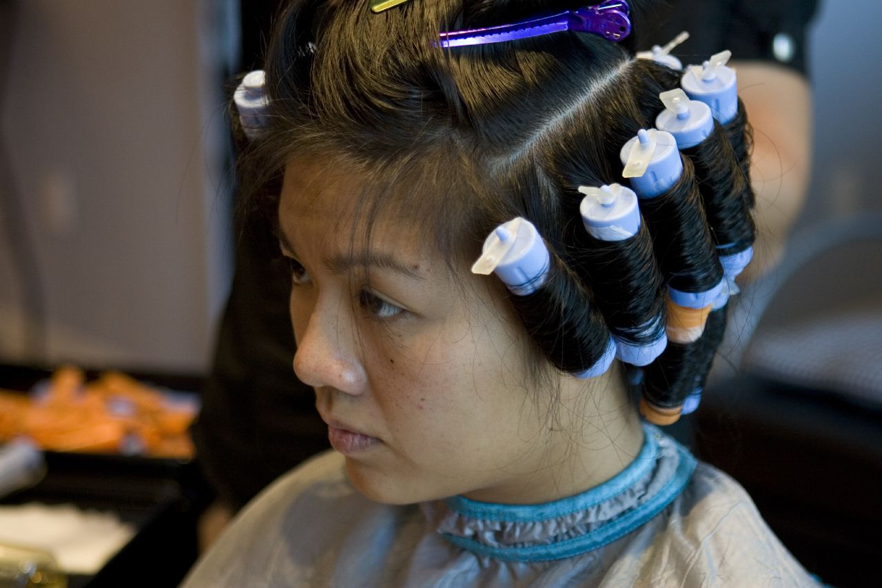 Person with hair in curlers seated in a salon chair, wearing a cape.