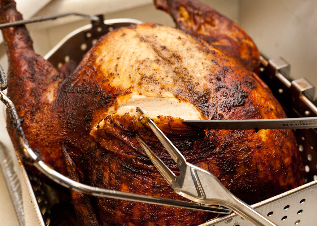 A close-up of a perfectly cooked turkey being expertly carved with a knife and fork in a metal roasting pan, capturing the golden skin reminiscent of a deep-fry technique.