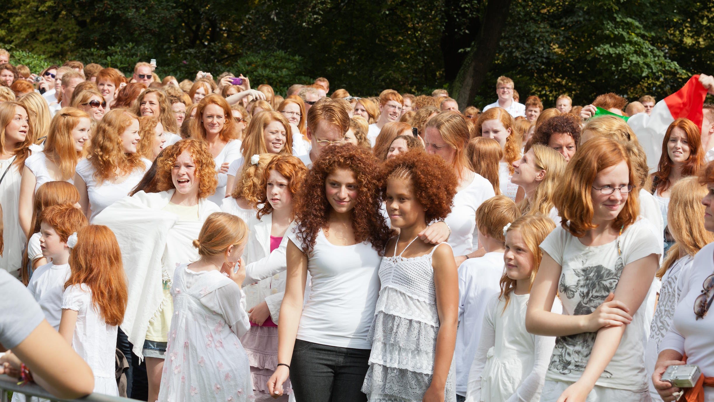 A large group of people with red hair gather outdoors, many wearing white clothing.