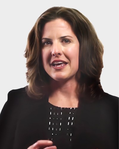 Woman speaking, wearing a black top, against a plain background.