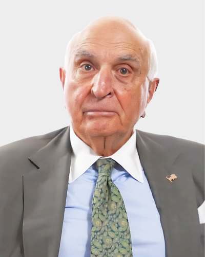 An older man in a suit and floral tie looks at the camera against a plain white background.