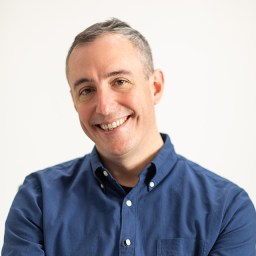 A person in a blue button-up shirt smiles against a plain background.