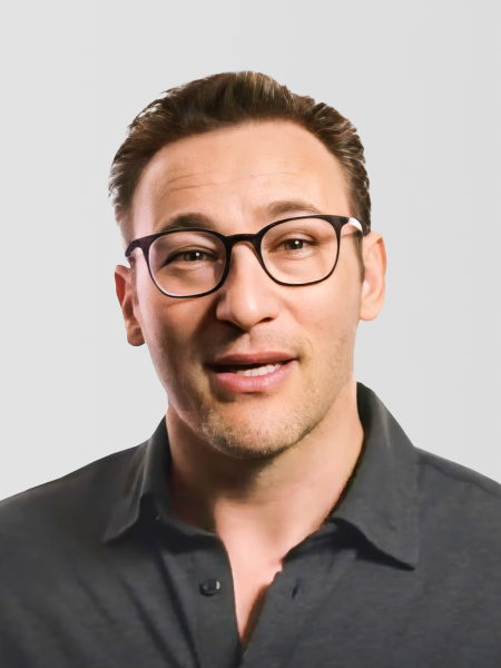 Simon Sinek wearing glasses and a dark shirt, speaking against a plain background.