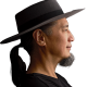 A man with a black ponytail and goatee wearing a wide-brimmed hat and black shirt is shown in profile against a dark background.