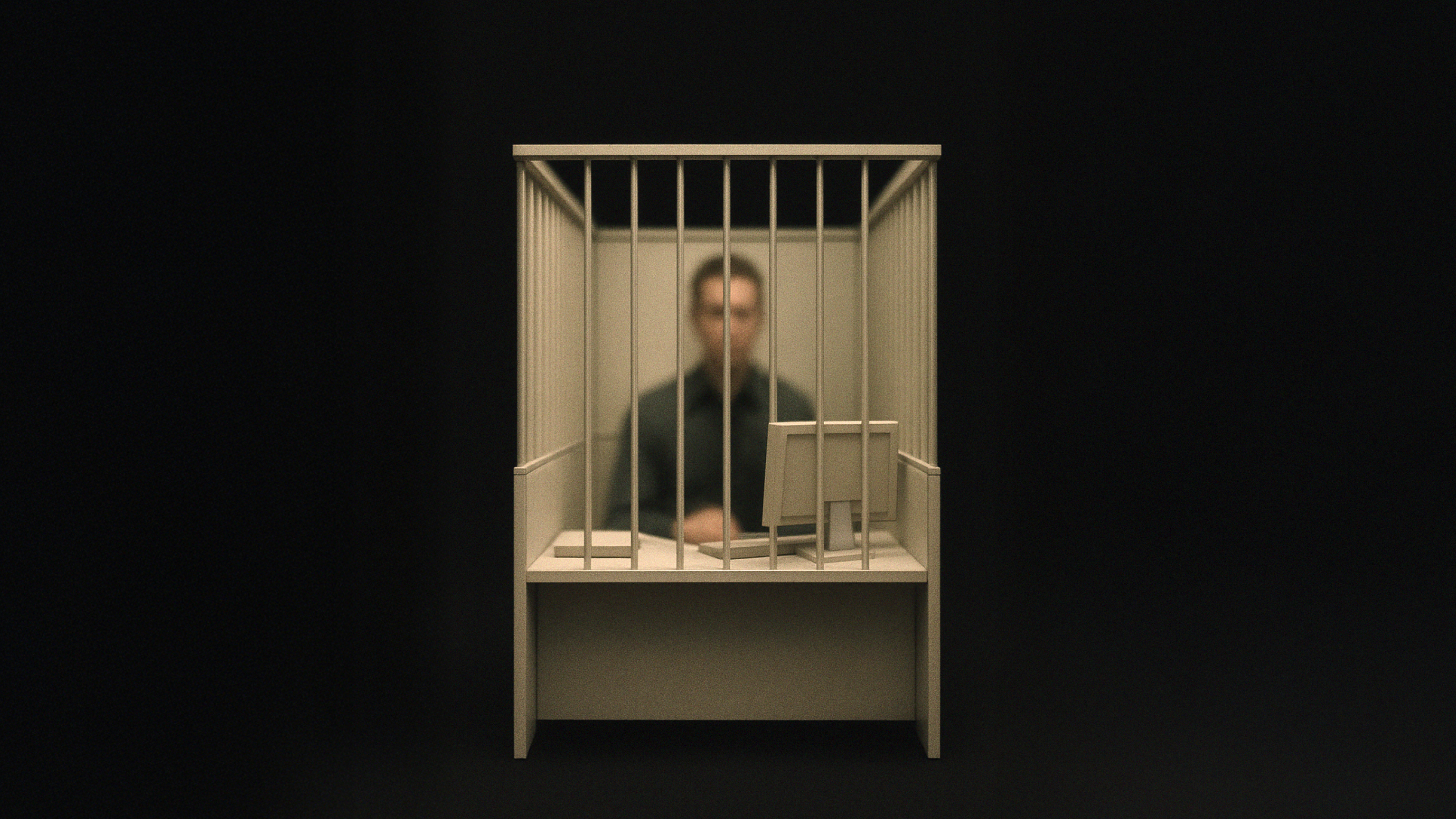 A person sits behind bars at a desk with a computer in a dimly lit setting, suggesting restriction or confinement.