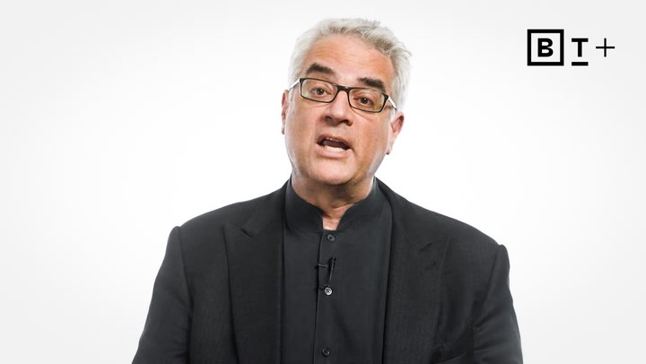 A man with gray hair and glasses wearing a black suit and shirt speaks in front of a white background with the BT+ logo in the top right corner.