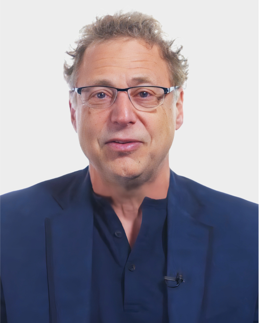 A middle-aged man with glasses and curly hair is wearing a dark jacket and shirt, facing the camera against a plain white background.