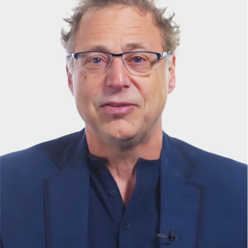 A middle-aged man with glasses and curly hair is wearing a dark jacket and shirt, facing the camera against a plain white background.