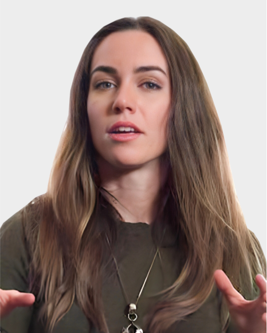 Woman with long brown hair wearing a dark top and necklace, speaking with hands raised against a plain light background.