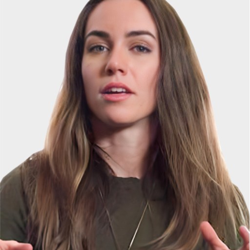 Woman with long brown hair wearing a dark top and necklace, speaking with hands raised against a plain light background.