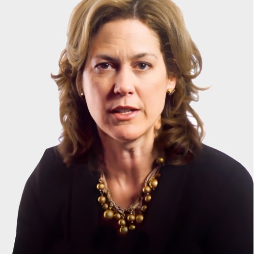 A woman with wavy brown hair wearing a black top and a gold bead necklace, looking directly at the camera with a neutral expression.